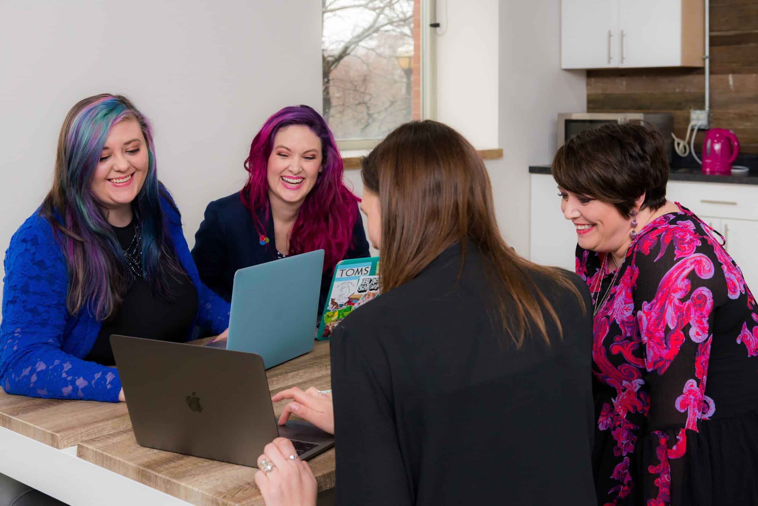 4 women smiling looking at a laptop