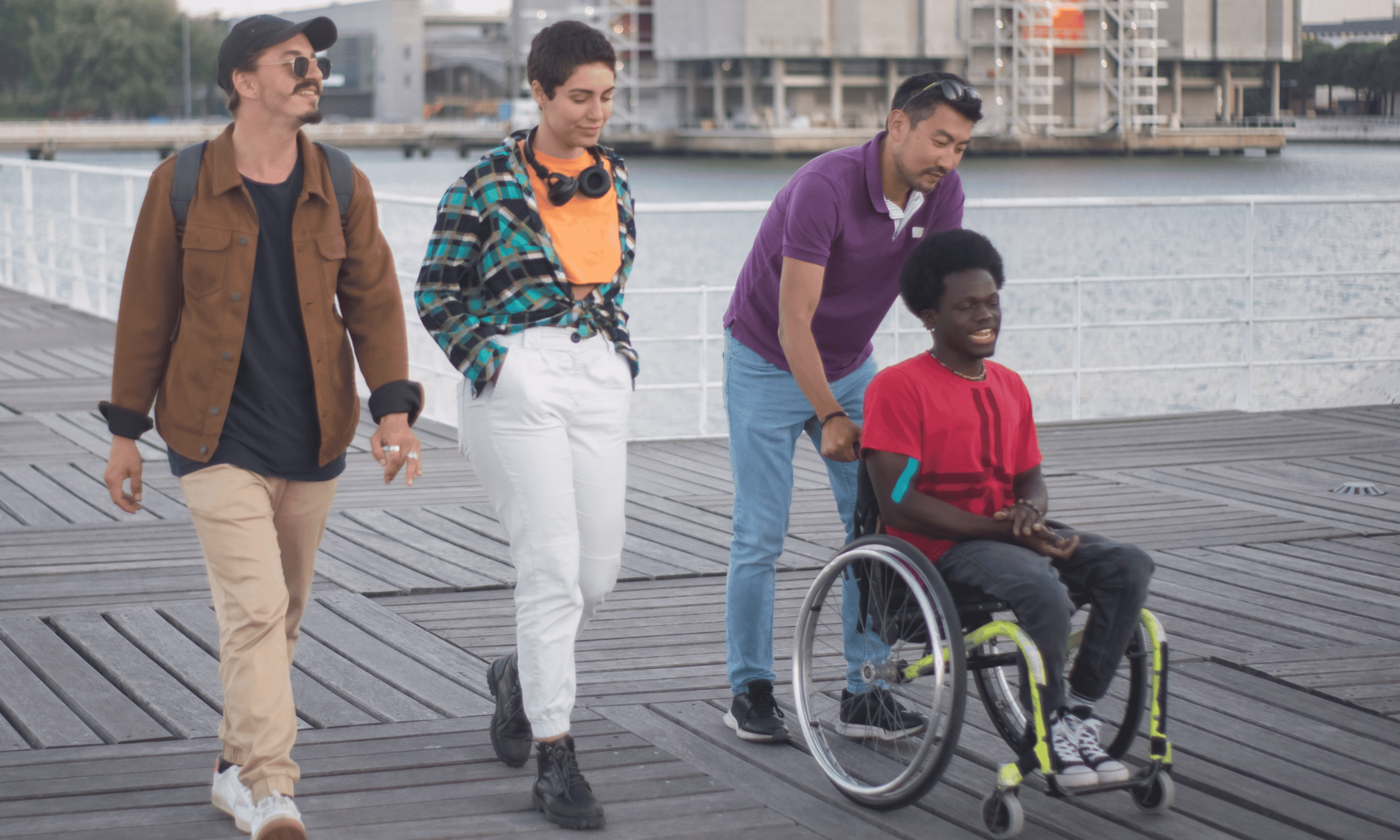 Male and female walking a third male walking and pushing a fourth male in a wheelchair